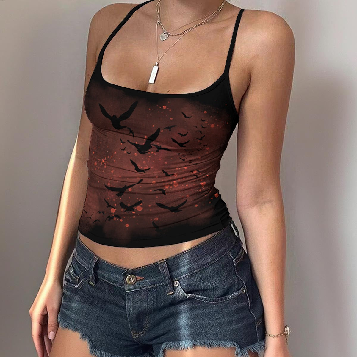 Person wearing a black tank top with bird design and denim shorts against a neutral background