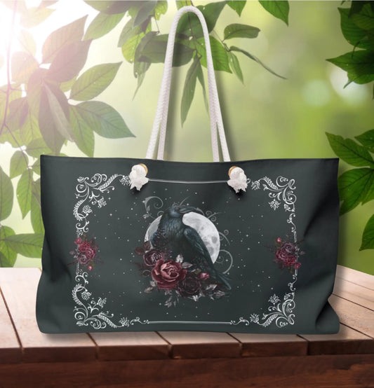 Black tote bag with a bird and floral design on a wooden surface with green leaves in the background