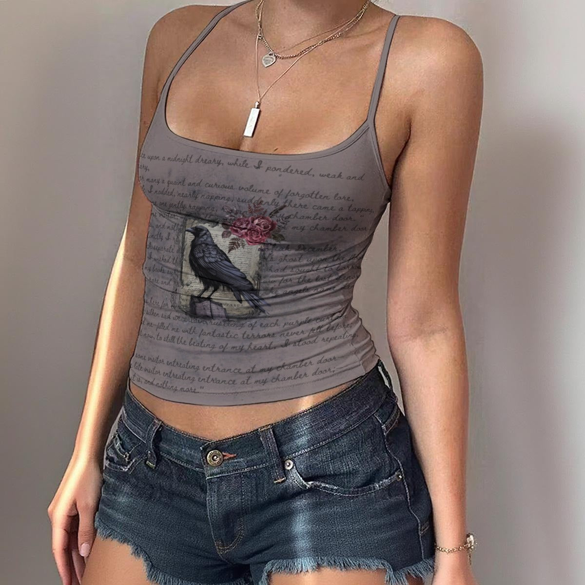 Person wearing a gray tank top with a graphic design and denim shorts against a plain background