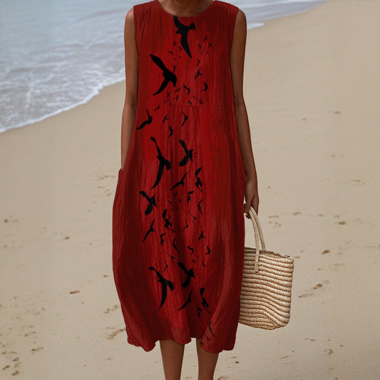 Person wearing a red dress with black bird patterns on a beach.