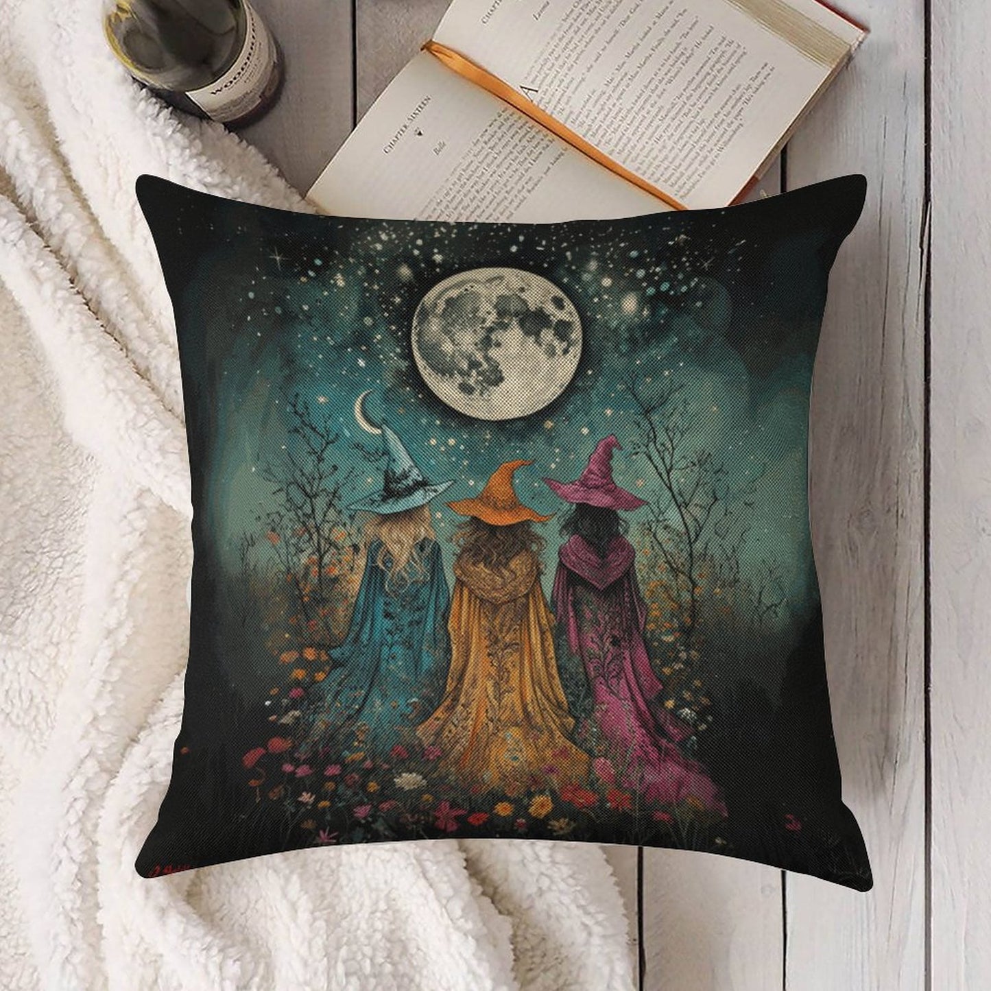 Decorative pillow with three witches under a moonlit sky on a white surface.