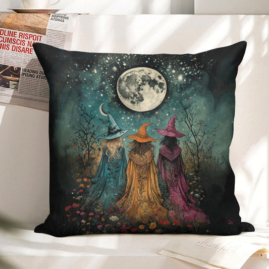 Decorative pillow with three witches under a moonlit sky on a white surface.