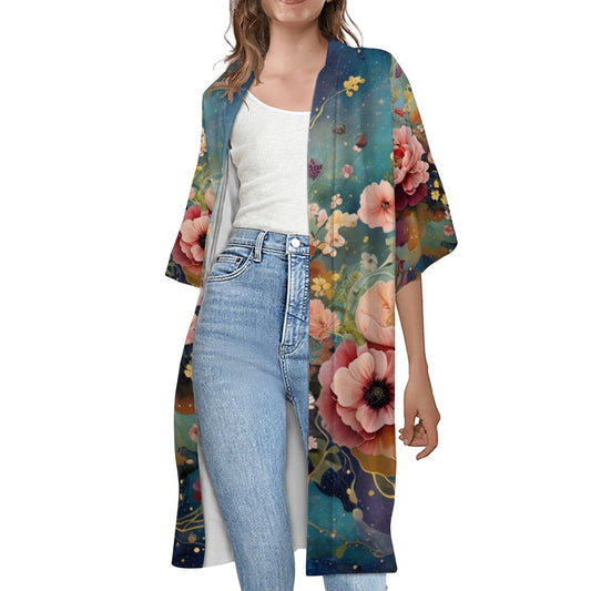 A woman wearing a multicolored floral short sleeve cape with a white top and blue jeans.