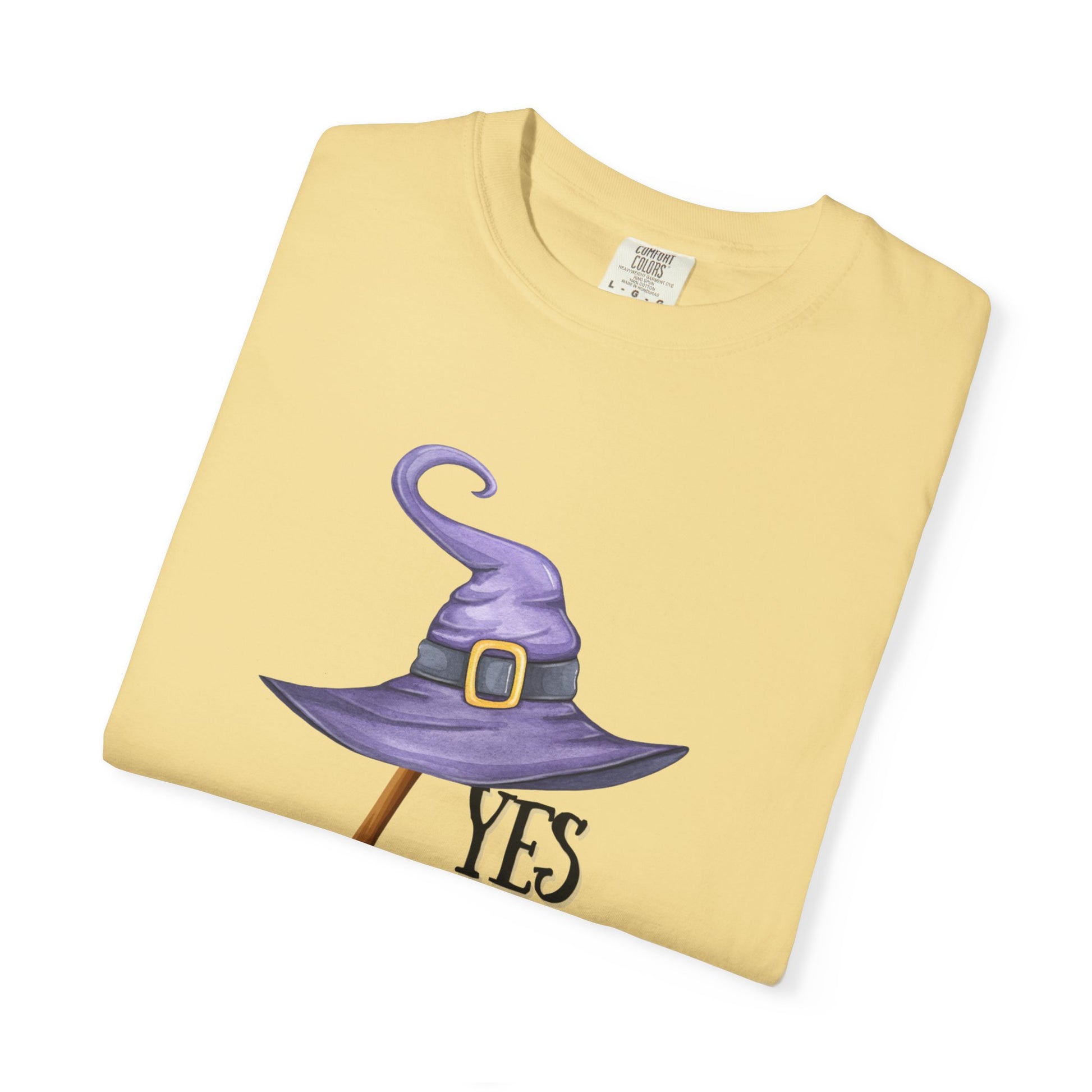 Folded yellow t-shirt with a purple witch hat graphic and 'YES' text on a white background