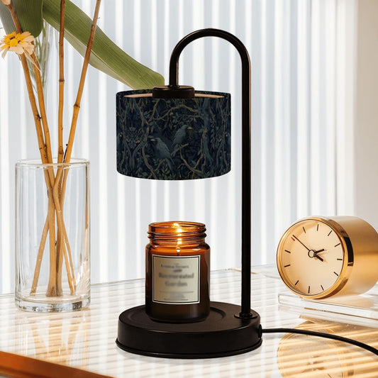 Black table lamp with a dark floral-patterned shade, amber candle jar, and gold clock on a reflective surface.