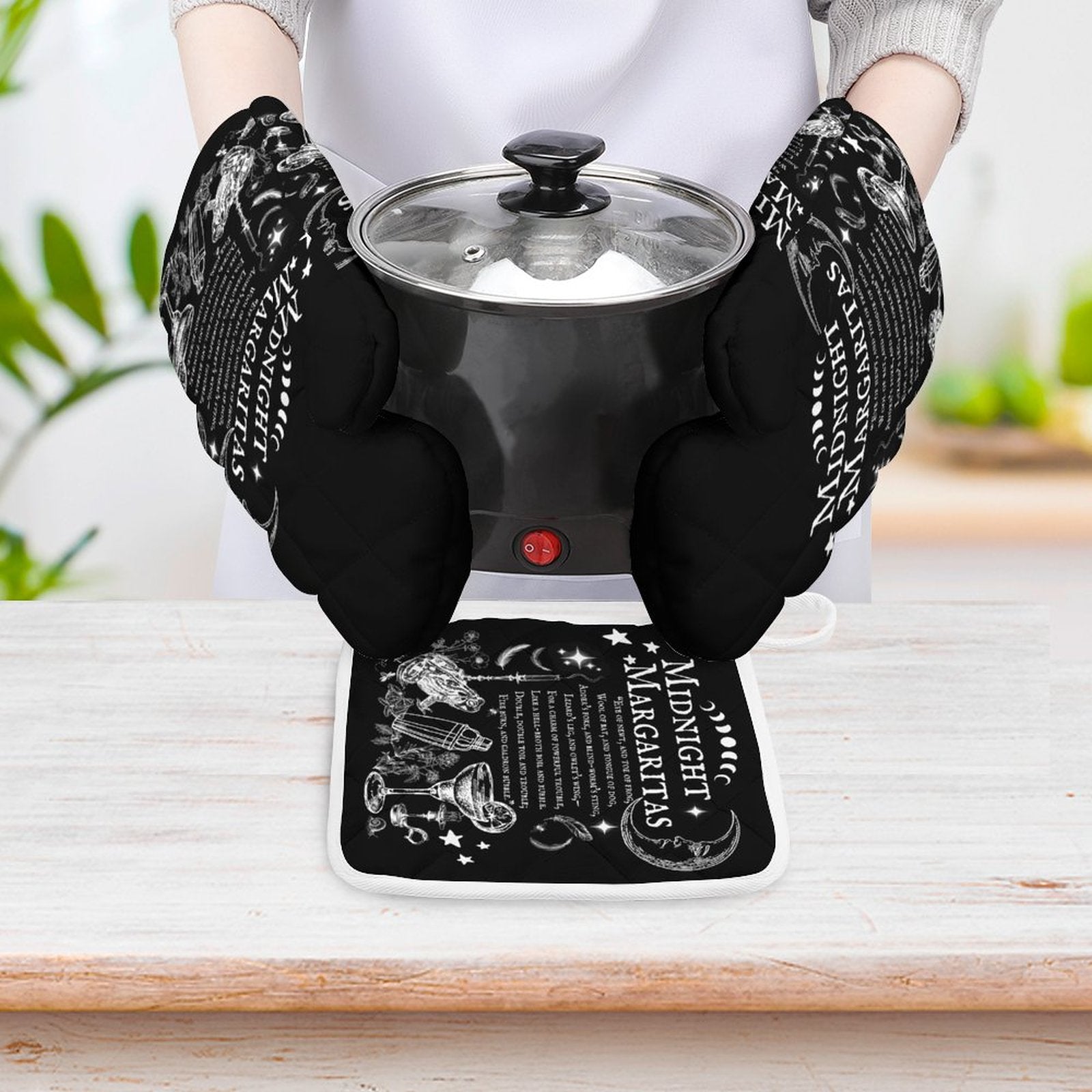 Person holding a black electric hot plate with a glass lid, wearing black gloves with white text.