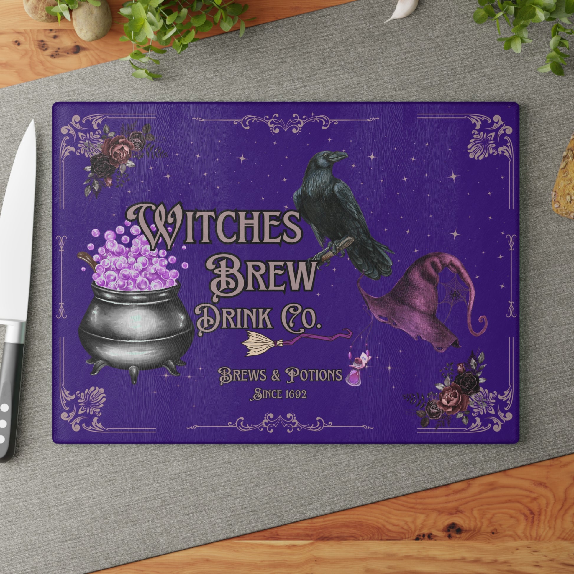 Purple cutting board with witch-themed design featuring a cauldron, raven, and hat on a gray surface.