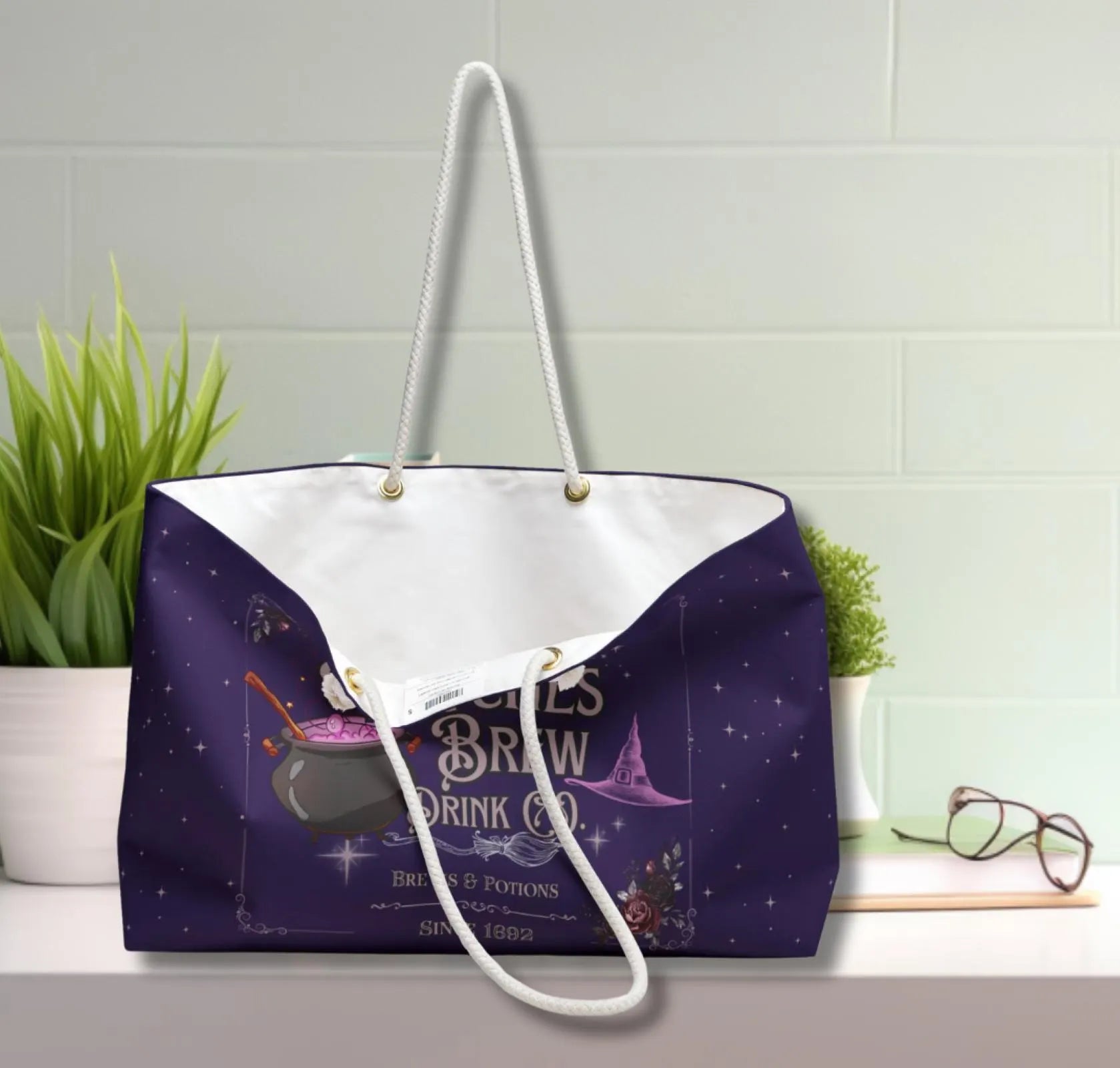 Purple tote bag with white handle on a light gray surface with plants and glasses in the background