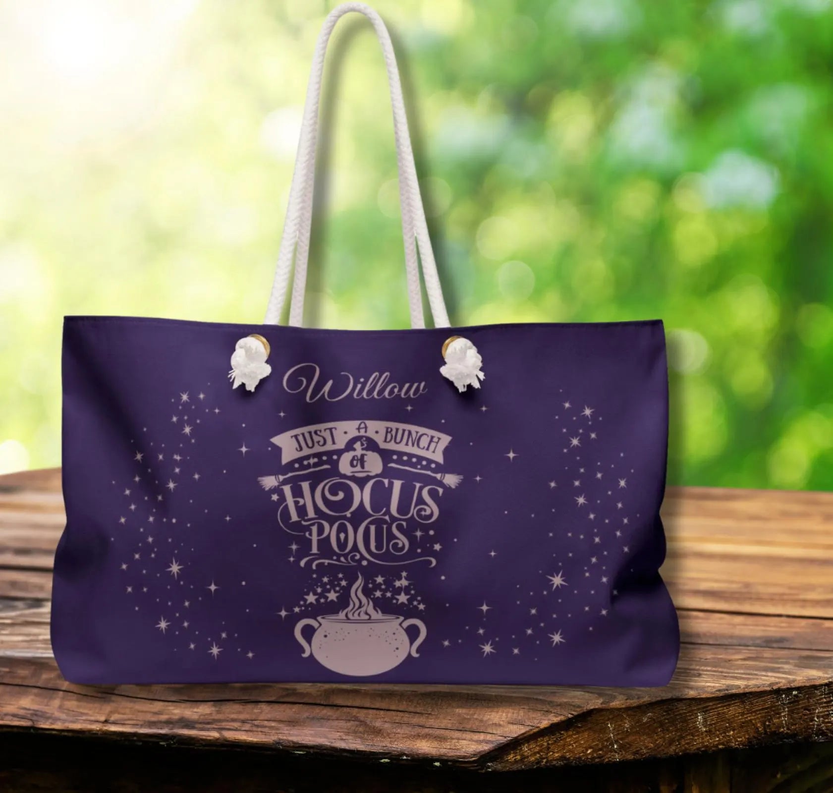 Purple tote bag with decorative text and design on a wooden surface with a blurred green background