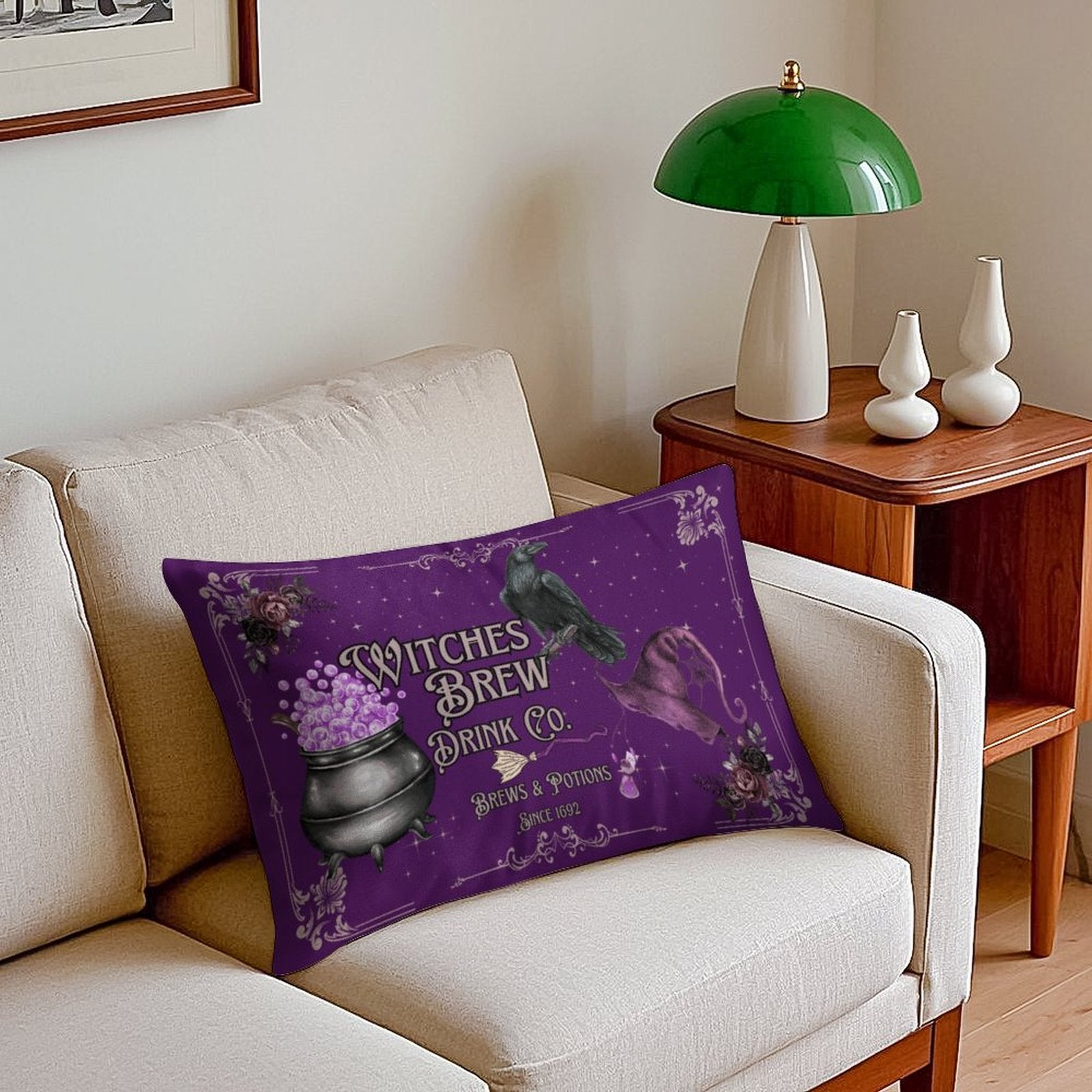 Purple pillow with witch-themed design on a beige sofa, green lamp in the background