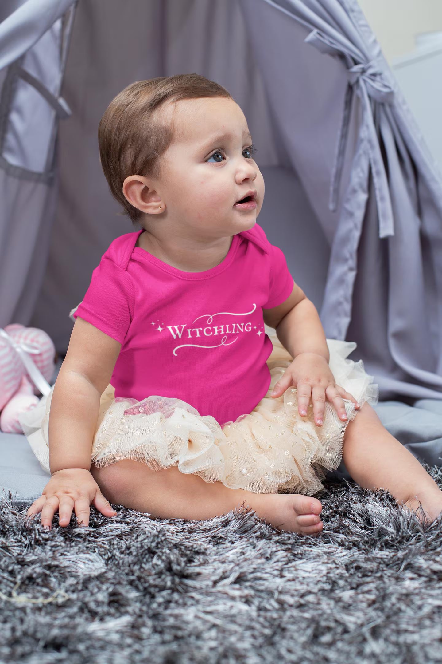 Baby wearing a pink onesie with text, sitting on a textured surface.