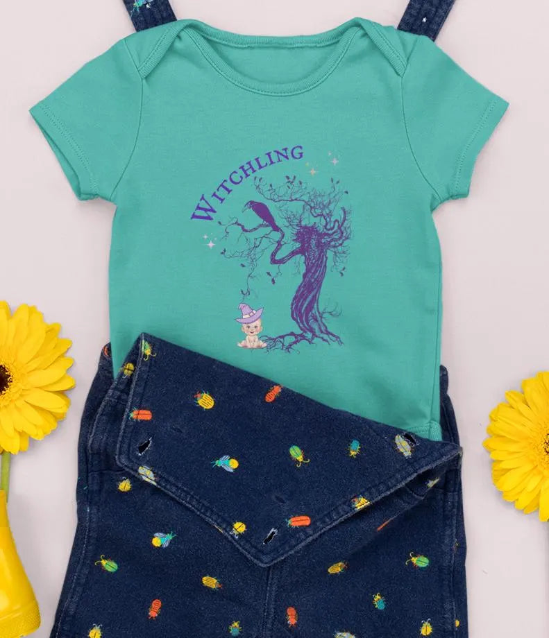 Green baby onesie with 'Witchling' design and blue jeans with colorful patterns on a white background.