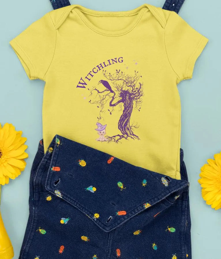 Yellow baby shirt with 'Witchling' design and blue overalls on a light blue background
