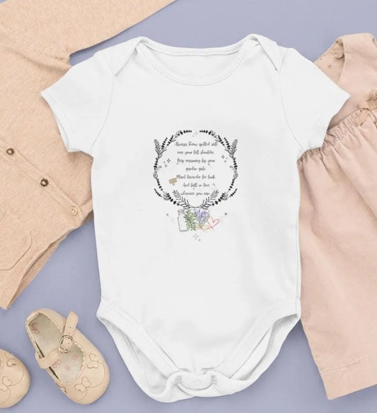 White baby onesie with floral design and text on a purple surface with baby items around
