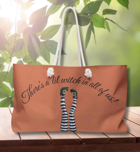 Tote bag with witch-themed design and text on a wooden surface with greenery in the background