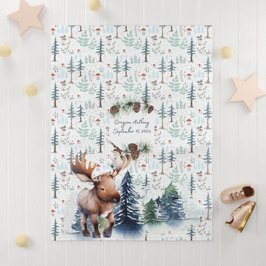 Baby shower blanket with moose and forest design on a white wooden surface.